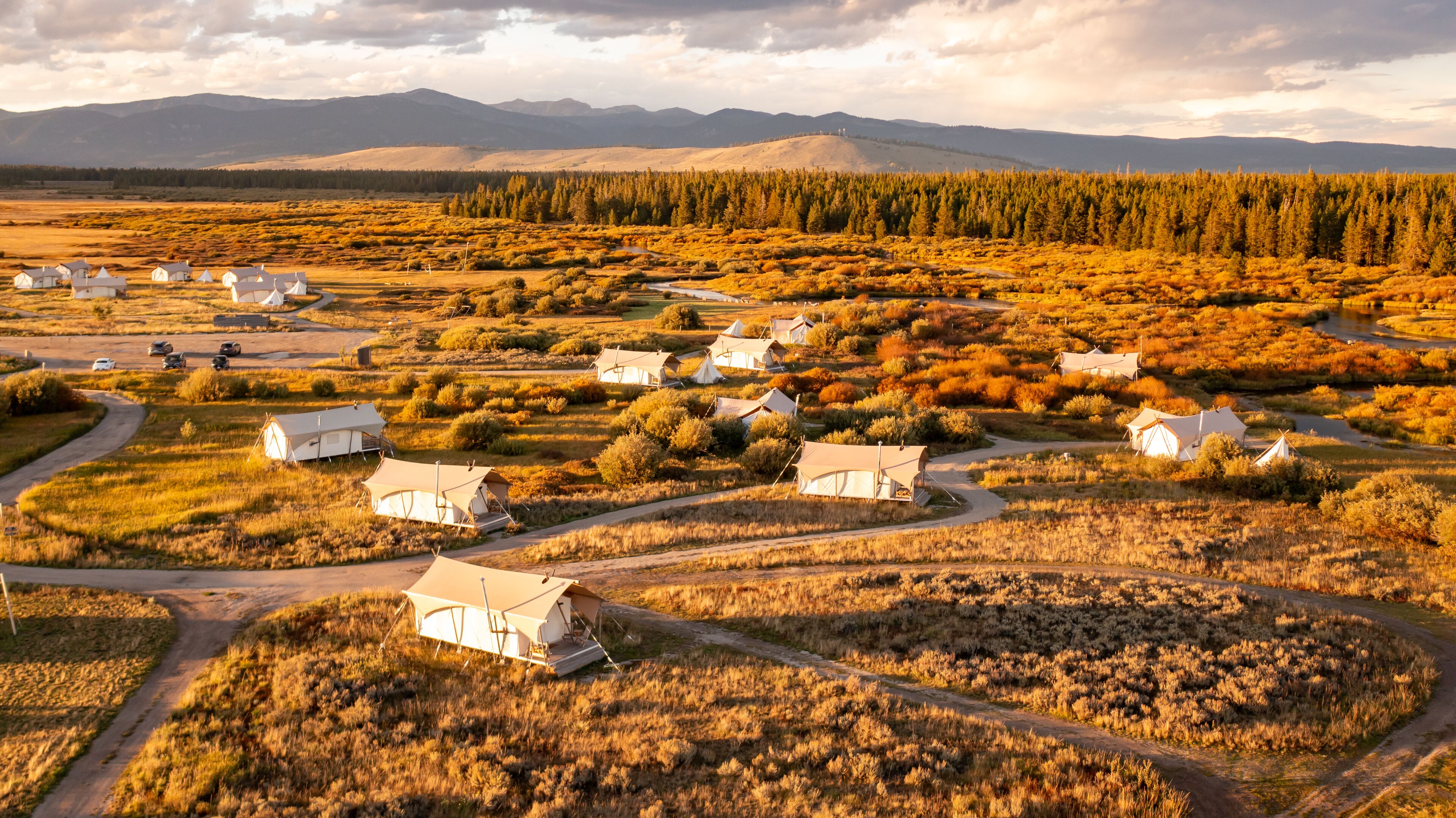Un camping aislado con varias tiendas de campaña dispuestas en semicírculo, rodeado por un paisaje natural con vegetación escasa y montañas a lo lejos.