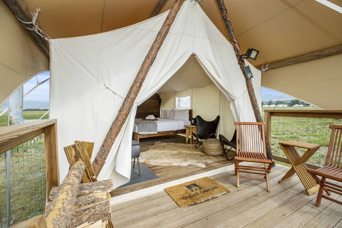 A tented accommodation with a bed, wooden furniture, and a view of the outdoors.
