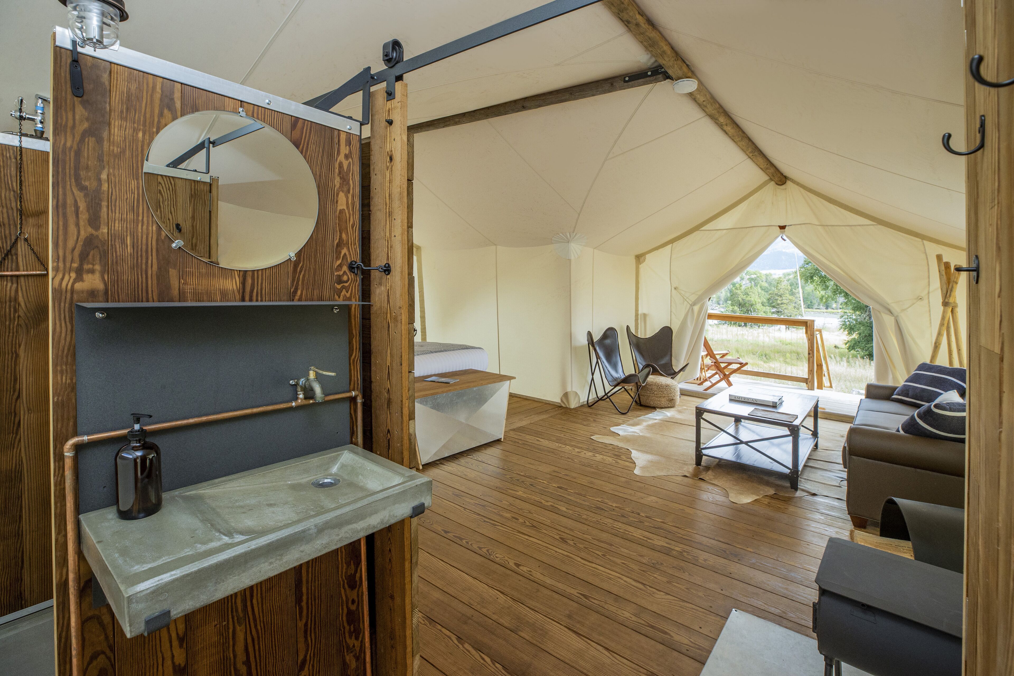 A tented accommodation with a wooden interior, a sink, mirror, and seating area.