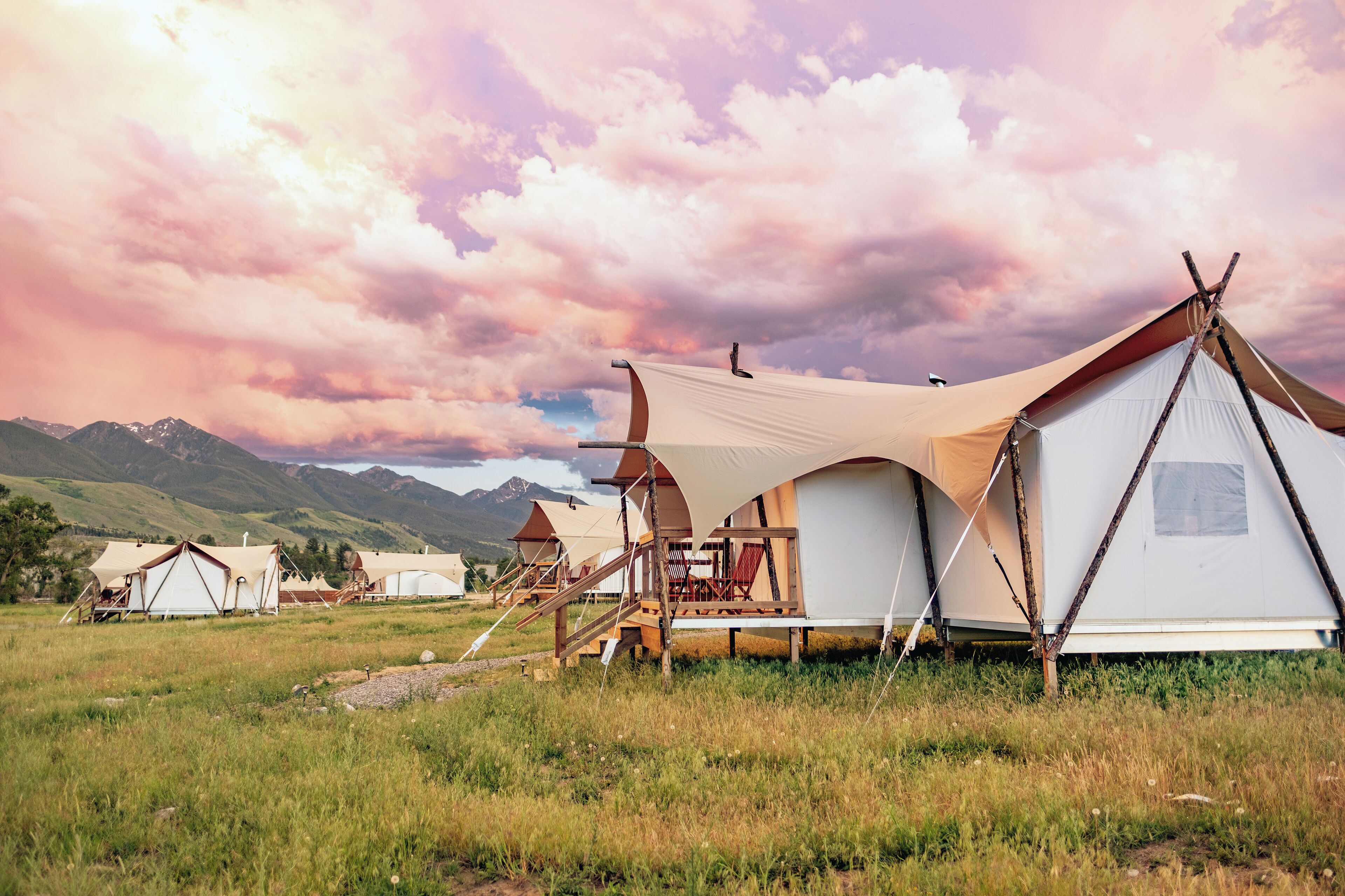 A series of tents in a grassy field with mountains in the background.