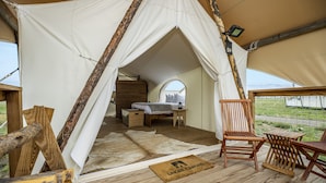 Eine Zelthatung mit einem Bett, Holzmöbeln und Blick ins Freie.