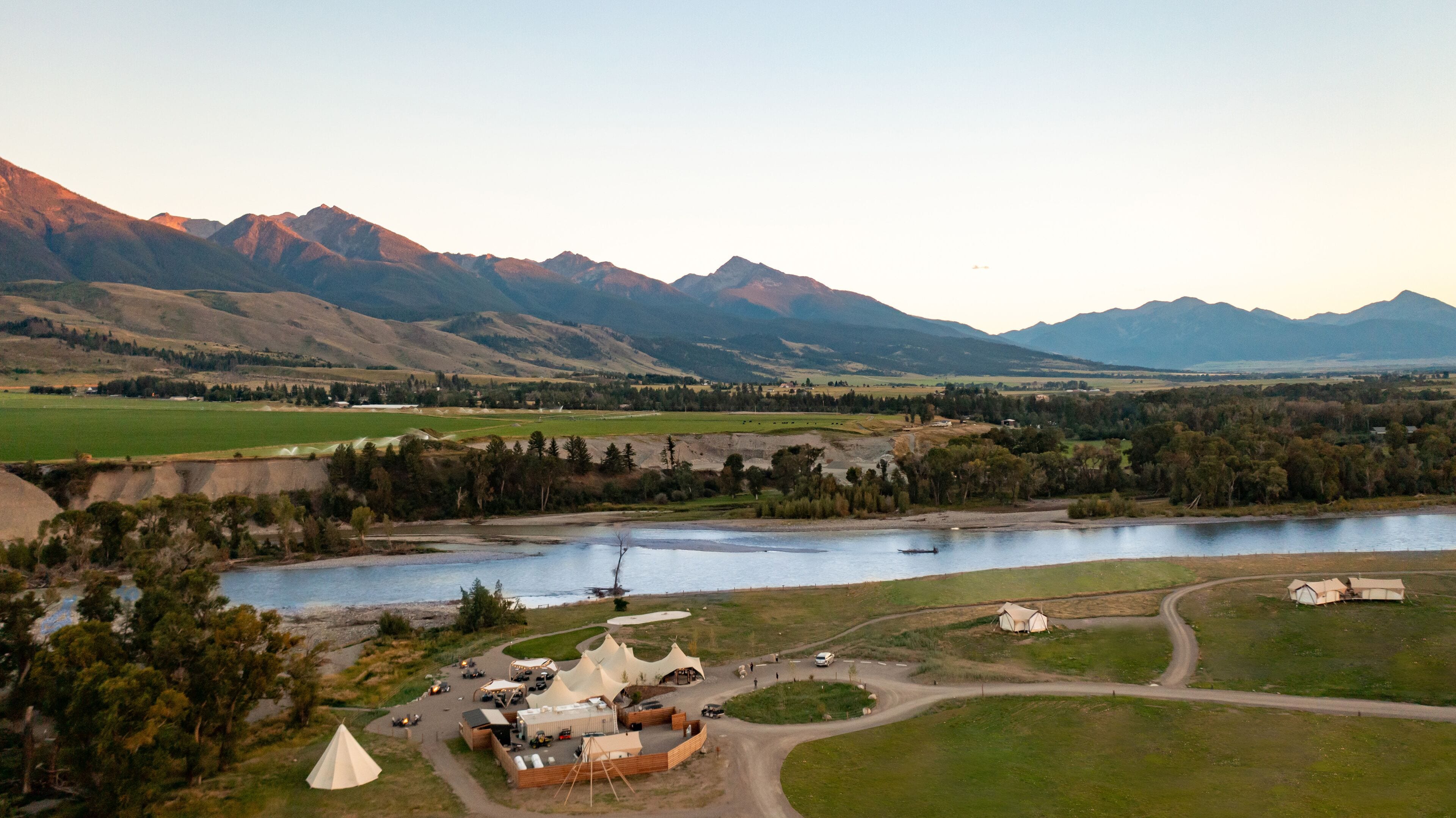 A campsite with tents and a small building, surrounded by a lake and mountains.