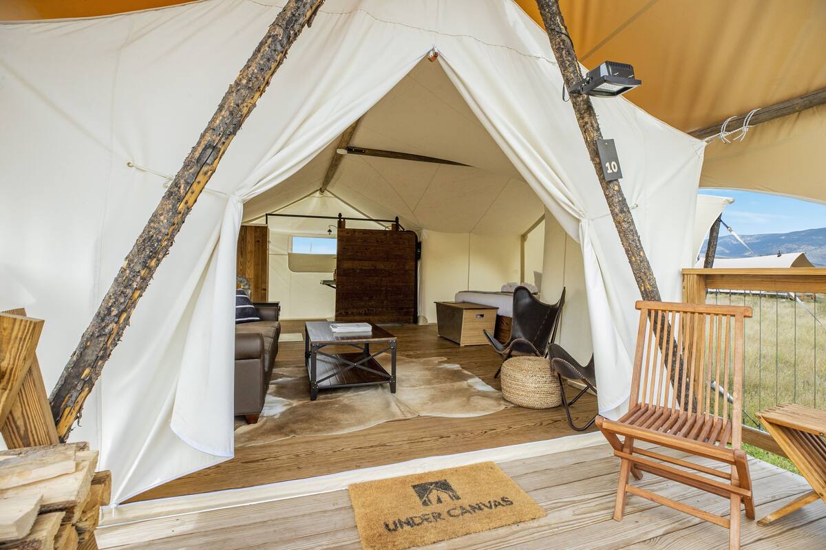 A tent with a wooden interior, including a table, chairs, and a sofa.