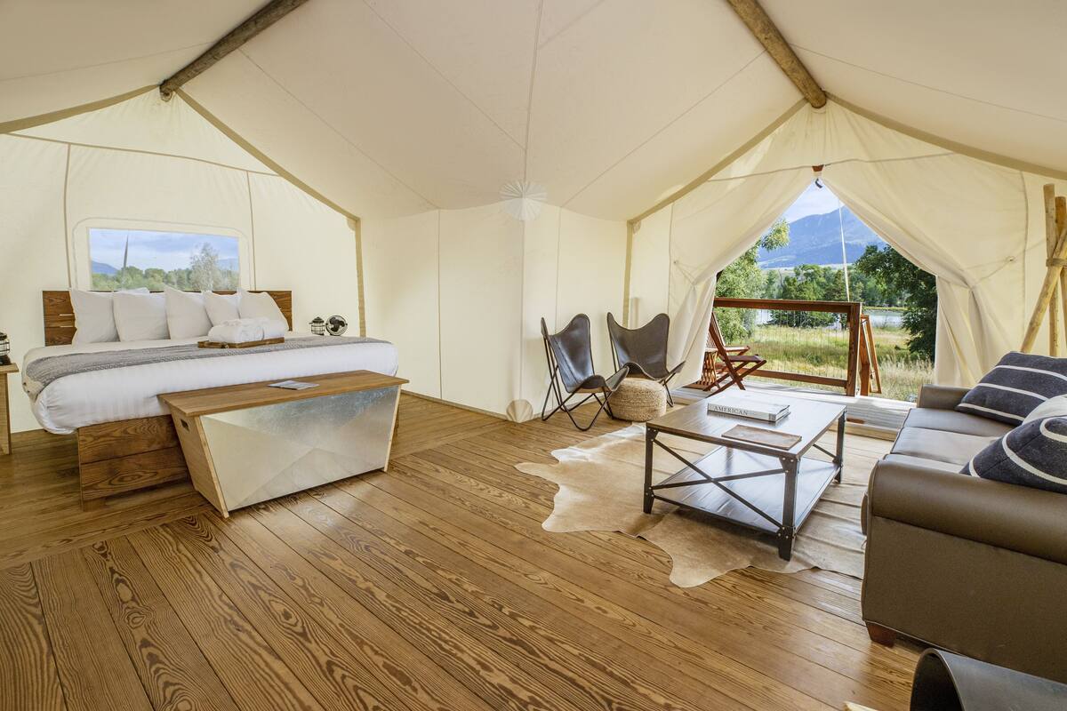 A tented accommodation with a bed, a sofa, a coffee table, and a view of the outdoors.