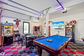 A pool table, arcade machines, and a snack vending machine in a room with a checkered floor.