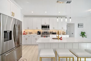 A modern kitchen with white cabinetry, stainless steel appliances, and a central island with stools.