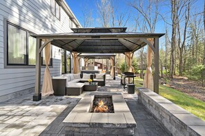 Un espacio de estar al aire libre cubierto con una chimenea, asientos acolchados y una pérgola.
