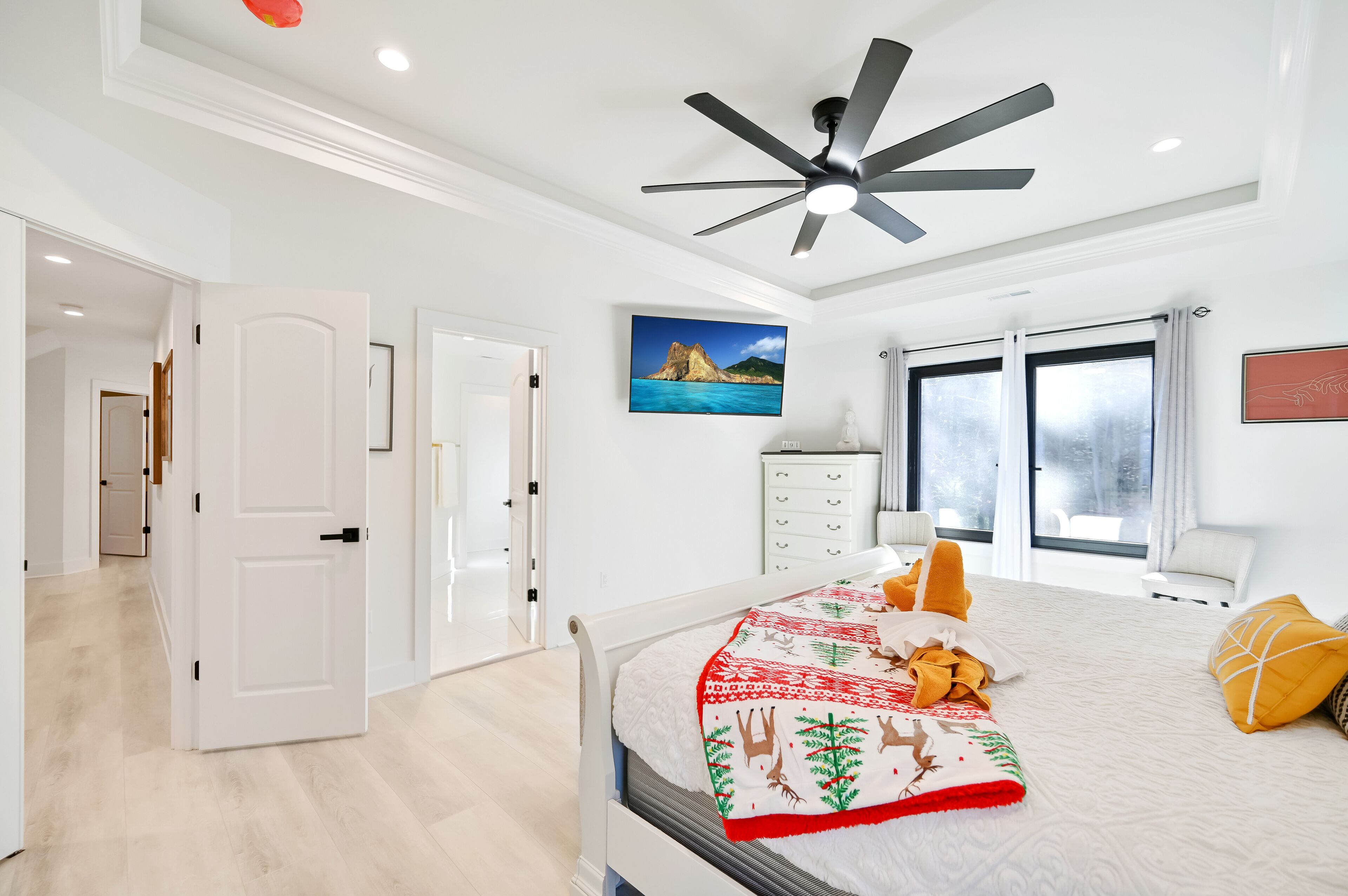 A modern bedroom with a bed, a ceiling fan, a nightstand, a window with curtains, and a painting on the wall.