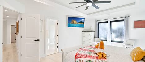A modern bedroom with a bed, a ceiling fan, a nightstand, a window with curtains, and a painting on the wall.