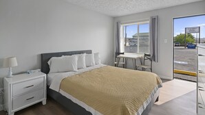 Ein Schlafzimmer mit Bett, Nachttisch, Lampe und Blick auf die Straße durch ein Fenster.