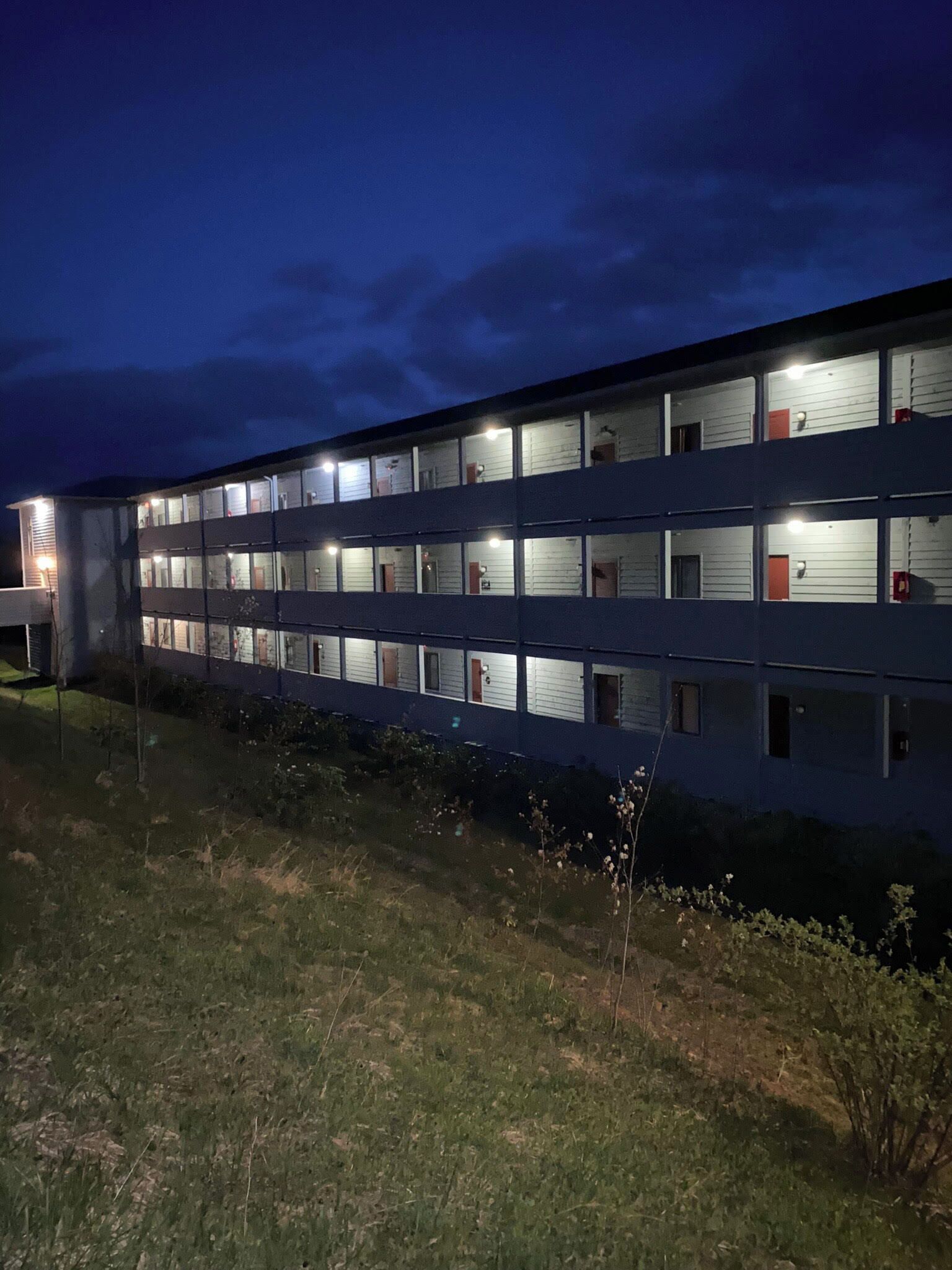 A multi-story building with individual rooms, each with a window and a door, and a flat roof.