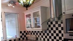A kitchen with white cabinets, a black and white checkered backsplash, a stainless steel range hood, and a decorative chandelier. - baroque villa (Pierrefitte-sur-Seine)