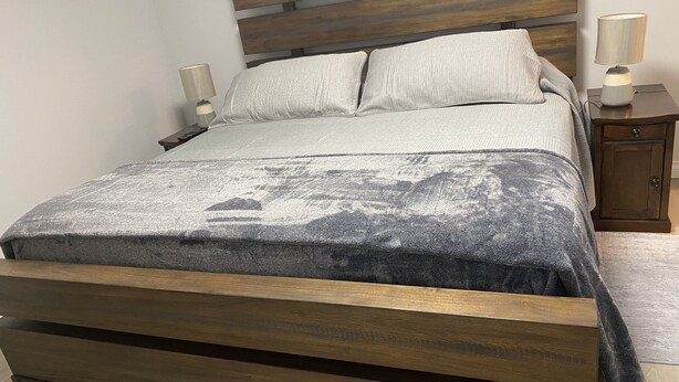 A bed with a wooden frame, a grey blanket, and two bedside lamps. - Classy, Comfy and Cozy (Timmins)