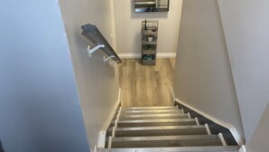 A staircase with a wooden finish and white handrails, leading to a landing with a mirror and a small shelf with decorative items. - Classy, Comfy and Cozy (Timmins)