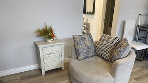 A living room with a round grey sofa, two patterned cushions, a small white side table with a plant, and a mirror on the wall. - Classy, Comfy and Cozy (Timmins)