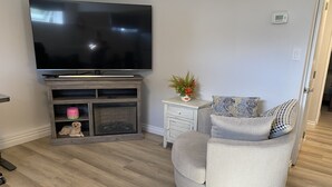 A living room with a flat-screen TV, a grey sofa with patterned cushions, a small side table with a plant, and a wooden entertainment unit with a dog figurine. - Classy, Comfy and Cozy (Timmins)