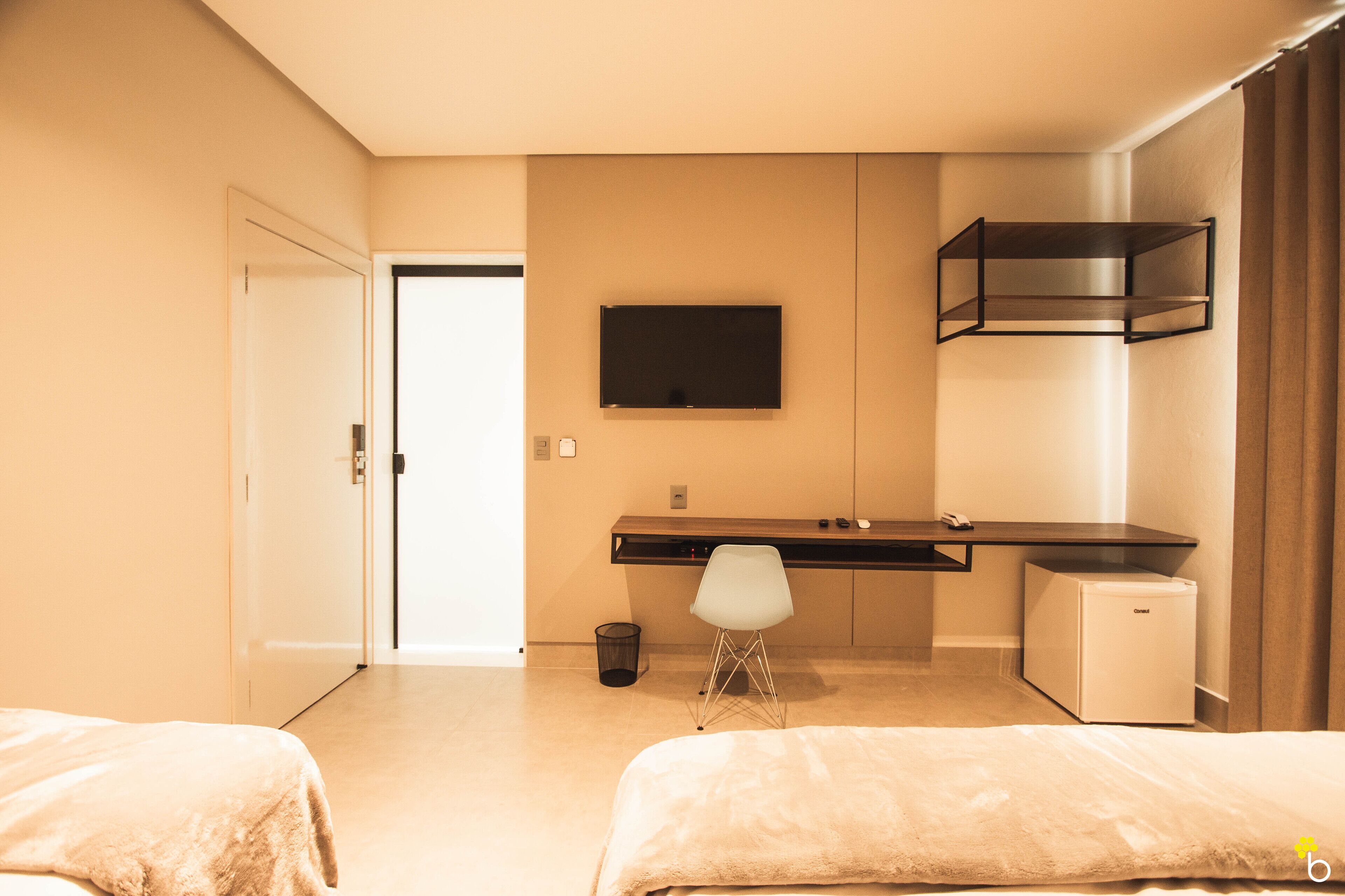 Une chambre d’hôtel équipée d’un lit, d’un bureau, d’une chaise, d’une télévision et d’un petit réfrigérateur.