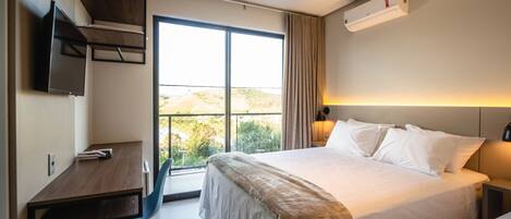 A hotel room with a bed, a desk, and a large window.