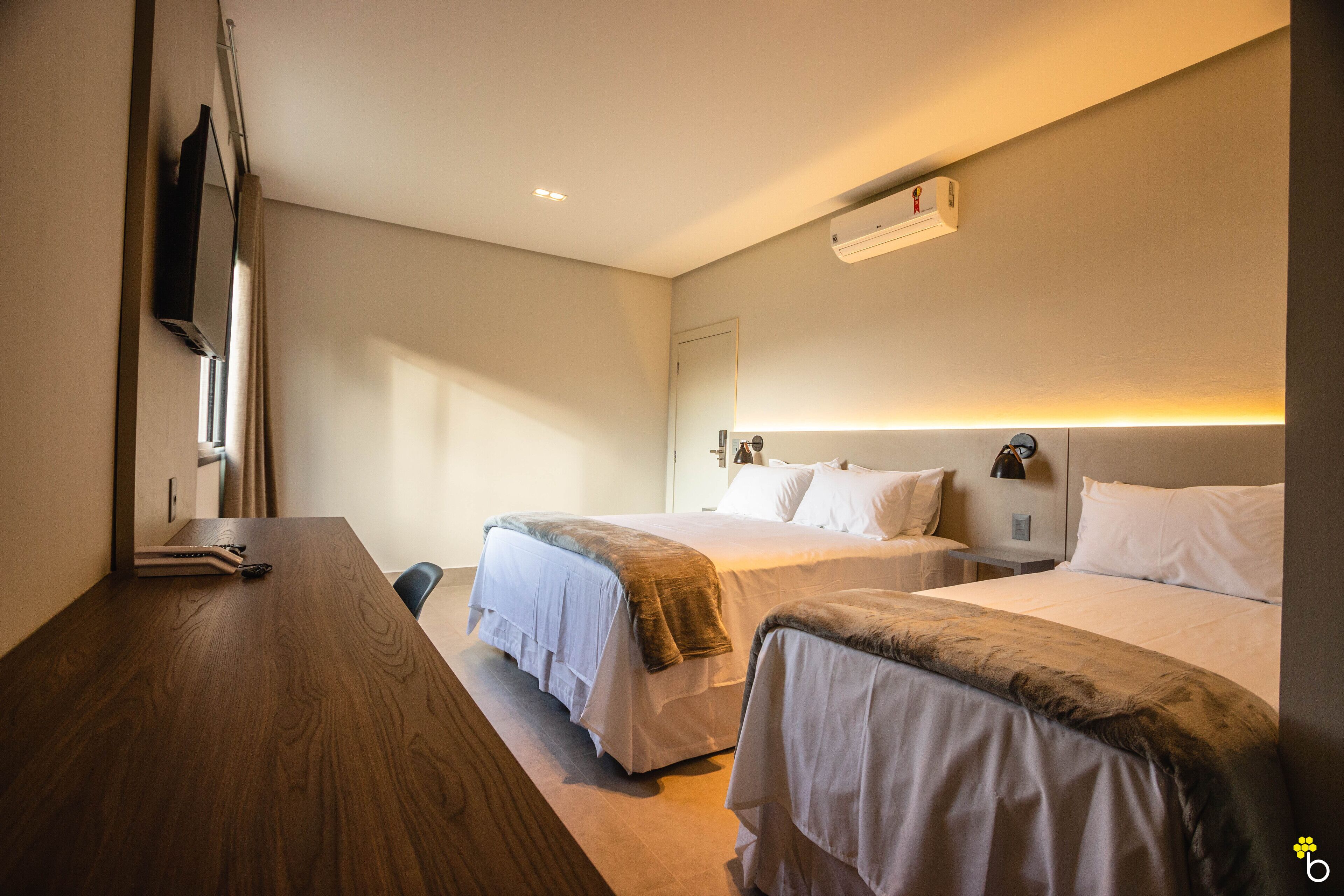Een hotelkamer met twee bedden, een houten bureau en een flatscreen televisie aan de muur.