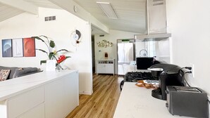 Een moderne keuken met witte kastjes, een houten vloer en een centraal kookeiland met een spoelbak en een koffieapparaat.