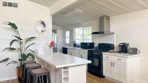 Een moderne keuken met witte kasten, een centraal eiland met krukken, een fornuis, magnetron en koffiezetapparaat.
