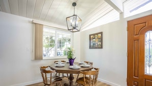 Een eetkamer met een houten tafel en stoelen, een hanglamp, een raam met gordijnen en een deur met ruit.