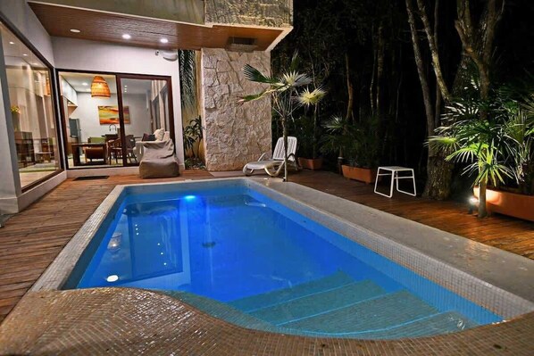 Una piscina con bordo in legno, parete in pietra e piante in vaso.