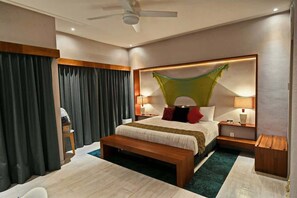 Camera d'albergo con un letto grande, lampade ai comodini, una panca, una ventola a soffitto e vista all'esterno.
