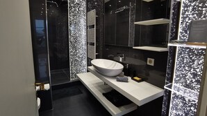 Un bagno moderno con un ampio lavandino bianco, box doccia in vetro e pavimento piastrellato di nero.