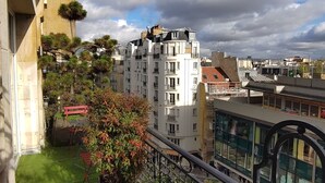 Un balcone con vista su un panorama urbano, che include un edificio a più piani e una struttura moderna con finestre in vetro.