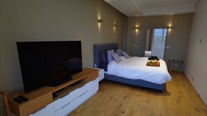 Una camera da letto moderna con una grande televisione a schermo piatto, un letto con piumone bianco e pavimento in legno.