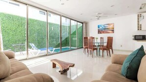 A modern living room with a large sliding glass door leading to a pool area, a wooden coffee table, and a dining set. - Wow! Gated House/WiFi/5 rooms/12 pax/Pool Private (Cancún)