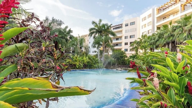 A pool surrounded by tropical plants and a multi-story building with balconies. - Wow! Gated House/WiFi/5 rooms/12 pax/Pool Private (Cancún)