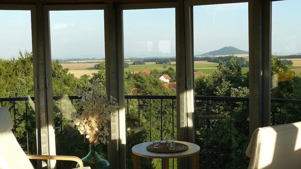 Un balcon donnant sur un paysage rural, un vase rempli de fleurs et deux chaises.