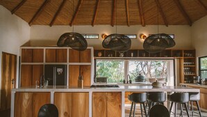 A modern kitchen with wooden cabinetry, a large island with bar stools, and pendant lighting. - La Musa de la Jungla (Nosara)
