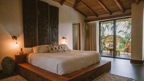 A spacious bedroom with a large bed, wooden headboard, and a view of the outdoors through a sliding glass door. - La Musa de la Jungla (Nosara)