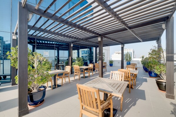 Une terrasse extérieure avec des tables et des chaises en bois, des plantes en pot et une structure vitrée.