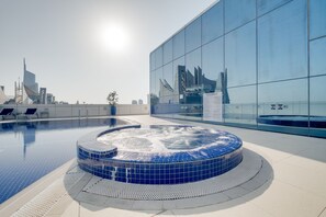 Une piscine intérieure moderne dotée d’un jacuzzi, entourée d’un mur de verre qui reflète le paysage urbain.
