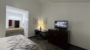 A hotel room with a bed, a desk, a television, and a bathroom with a mirror and lights.