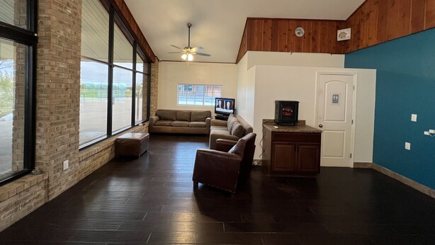 A spacious living room with a large window, a ceiling fan, a fireplace, and a television.