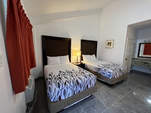 A hotel room with two beds, a nightstand with a lamp, a bathroom with a mirror, and a red curtain.