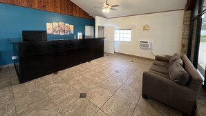 A reception area with a black counter, a ceiling fan, a blue wall with artwork, a white door, and a window with blinds.