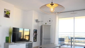 Uma sala de estar moderna com televisão de tela plana, geladeira, mesa de jantar e uma janela grande com vista.