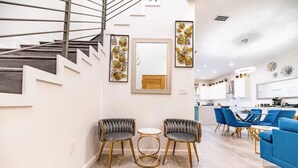 Un salon moderne avec un escalier, deux fauteuils gris à revêtement, une petite table ronde et un canapé bleu.