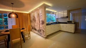 Una cocina moderna con armarios blancos, un comedor con mesa y sillas redondas, y un amplio ventanal con vista a zonas verdes.