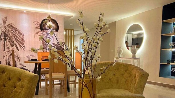 Una sala de estar moderna con una mesa redonda de madera, un sofá capitonado y un comedor con mesa y sillas.