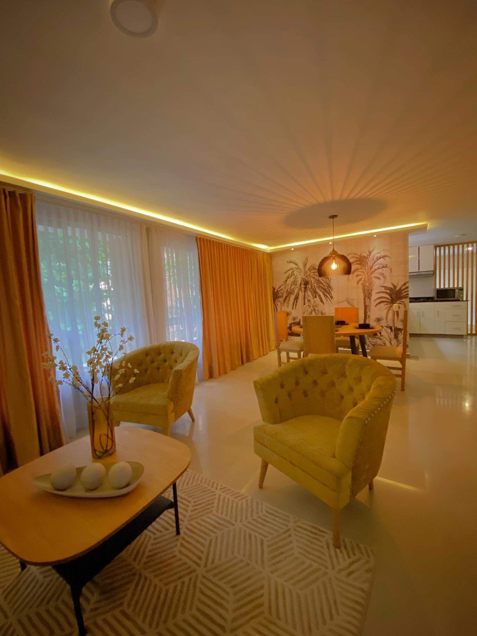 A modern living room with two yellow armchairs, a round coffee table, and a dining area with a table and chairs.