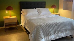 Una cama bien tendida con sábanas blancas en una habitación con paredes verdes y suelo de madera.