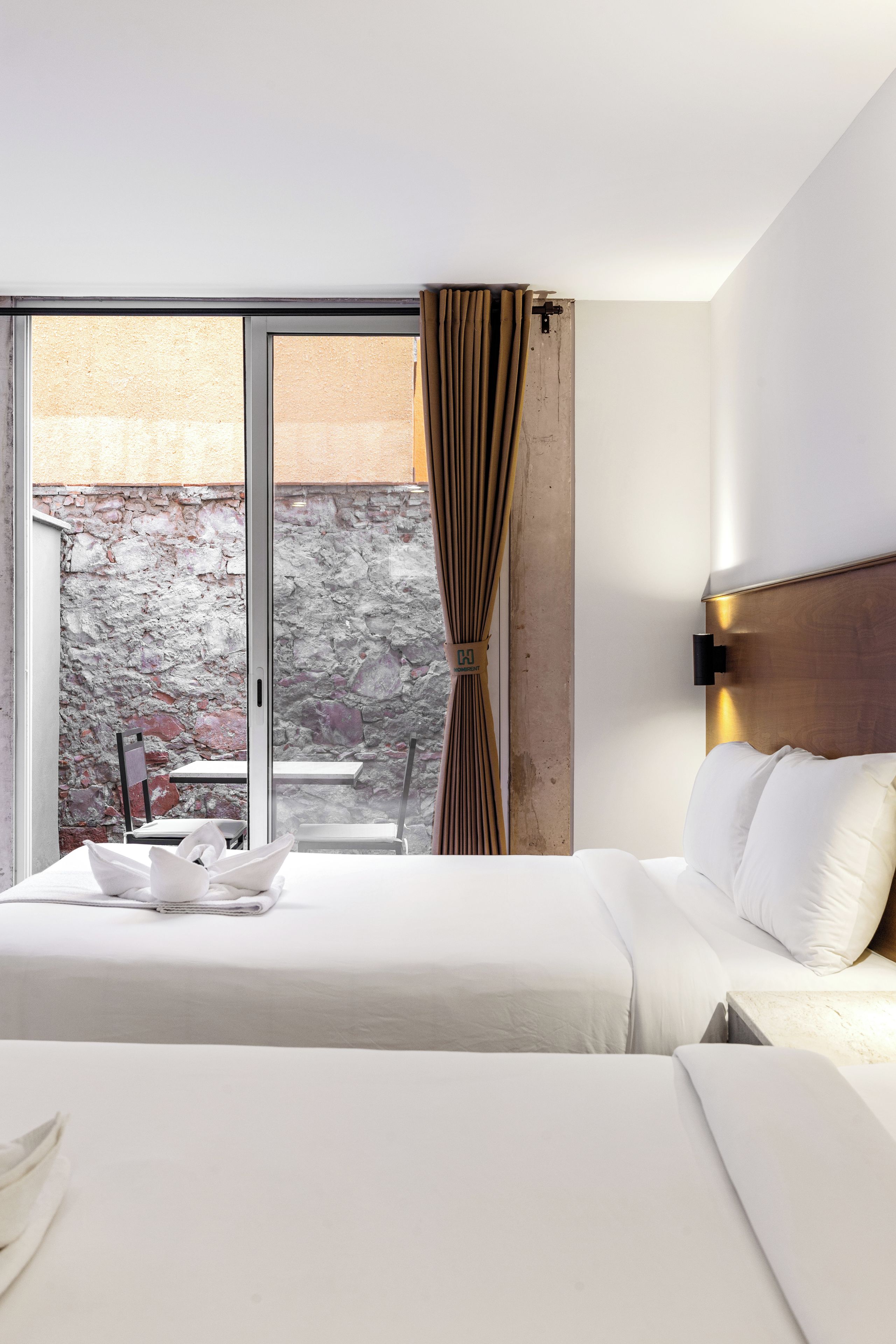 Habitación de hotel con una cama grande, vistas a un muro de piedra y un comedor visible a través de la ventana.