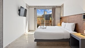 Ein modernes Hotelzimmer mit einem großen Bett, einem an der Wand befestigten Fernseher und einem Balkon mit Stadtblick.